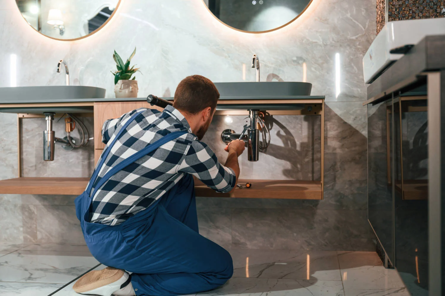 Busy by repairing siphon. plumber in blue uniform is at work in the bathroom